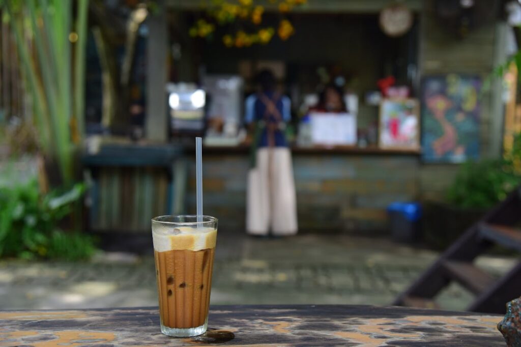 A refreshing iced coffee with a straw on a rustic table, cafe blurred in the background.
